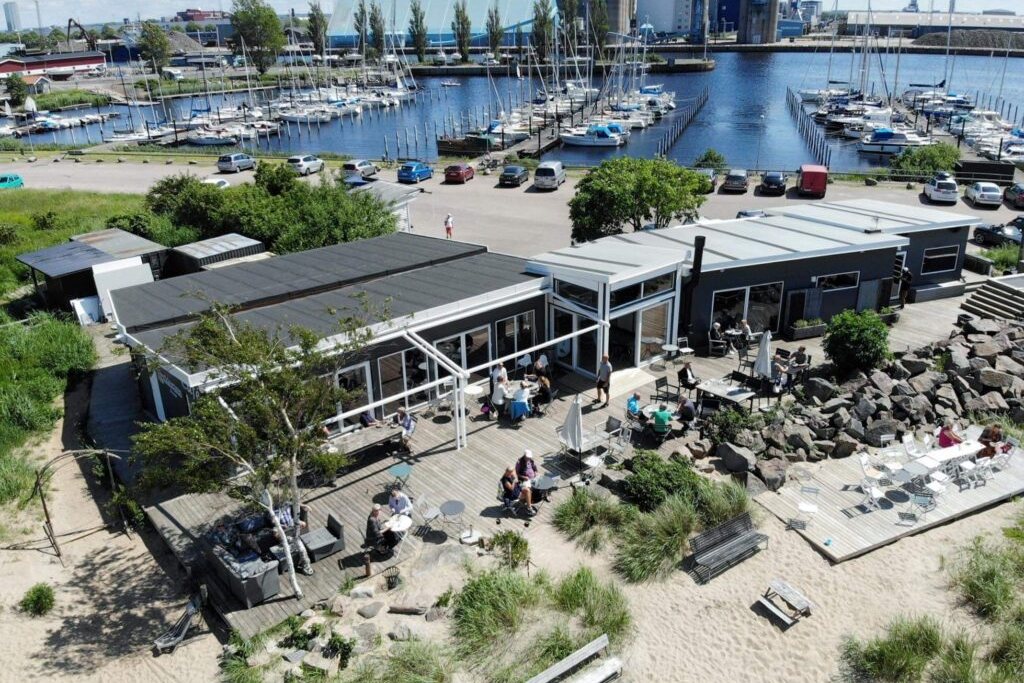 Caféets trädäck och uteserveringar vid stranden, med marinan i bakgrunden